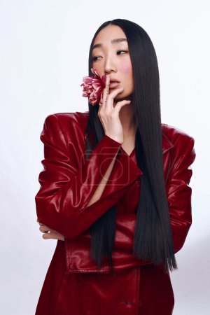 Foto de Mujer con estilo, pelo largo y negro, con chaqueta de cuero rojo y flor en la mano - Imagen libre de derechos