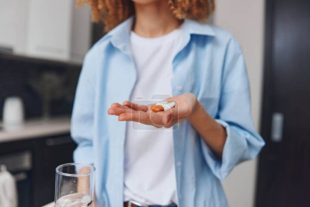 Mujer sosteniendo la píldora en la mano de pie delante de un vaso de agua listo para tomar la imagen concepto de medicación