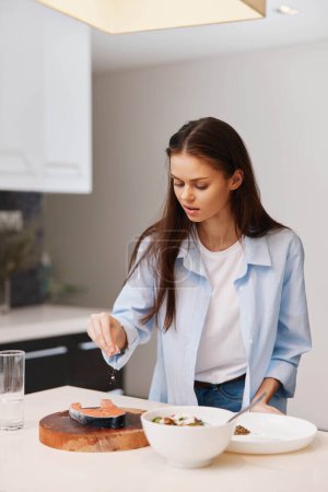 Foto de Woman in white shirt and blue jeans preparing food on kitchen table with various ingredients - Imagen libre de derechos