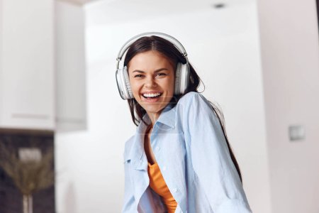 Foto de Mujer joven feliz disfrutando de la música con auriculares en la cocina en casa - Imagen libre de derechos