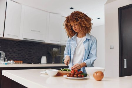 Photo for Woman preparing healthy vegetable salad in the kitchen with curly hair, organic ingredients in bowl - Royalty Free Image