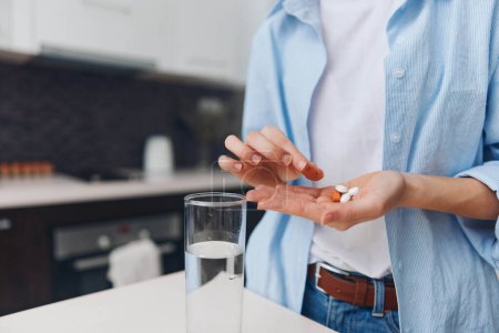Mujer sosteniendo una píldora en la mano preparándose para tomar medicamentos con un vaso de agua