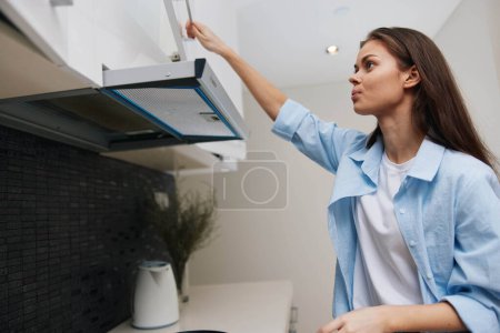 Téléchargez les photos : Femme en chemise bleue atteignant dans le four pour l'allumer et éteindre, concept de cuisson et de cuisson - en image libre de droit