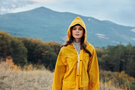 Foto de Mujer con impermeable amarillo de pie en campo sereno con majestuoso fondo de montaña Una instantánea de la belleza de las naturalezas - Imagen libre de derechos