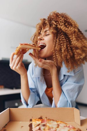 Junge Frau genießt ein leckeres Stück Pizza vor einer klassischen Pizzakiste mit lockigem Haar