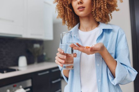 Frau mit lockigem Haar hält Glas Wasser und Tablette in der Hand, Konzept für Gesundheit und Wohlbefinden