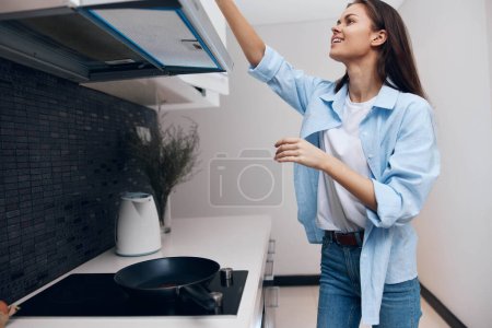 Woman in blue shirt cooking on stove with pan in kitchen at home