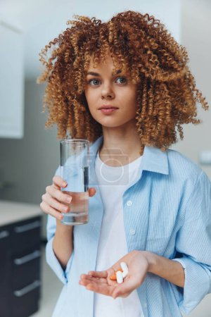 Frau mit lockigem Haar hält Glas Wasser und Tablette in der Hand, Gesundheits- und Hydratationskonzept