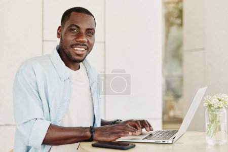 Téléchargez les photos : Homme assis à la recherche africaine adulte bureau américain sourire moderne heureux homme d'affaires de travail jeune personne ordinateur portable noir technologie entreprise masculine - en image libre de droit
