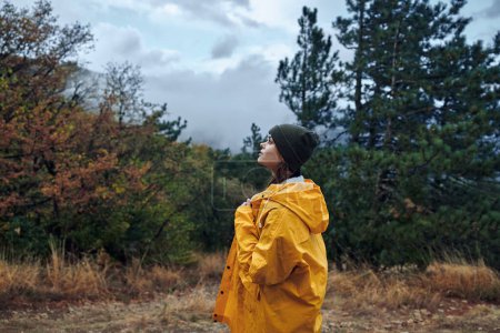Foto de Mujer con impermeable amarillo contemplando la naturaleza mientras camina por el bosque encantado durante la aventura del día lluvioso - Imagen libre de derechos