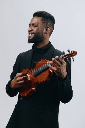 A man in dark attire passionately plays the violin against a clean white backdrop