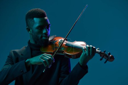 Téléchargez les photos : Élégant homme afro-américain en costume jouant du violon sur fond bleu créant une belle musique et de l'art - en image libre de droit