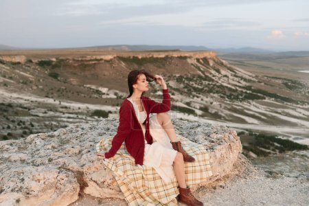 Foto de Woman sitting on rock in front of majestic mountains with background of peaks travel adventure concept photo - Imagen libre de derechos