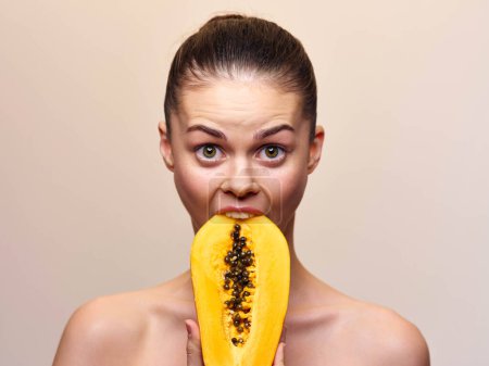 Foto de Mujer sorprendida con los ojos bien abiertos sosteniendo rebanada de papaya en la boca, vista de cerca de bocadillo de fruta saludable - Imagen libre de derechos