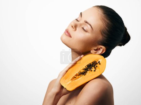 Téléchargez les photos : Modèle féminin attrayant posant avec des fruits de papaye sur la tête, isolé sur fond blanc pour le concept de beauté et de bien-être - en image libre de droit