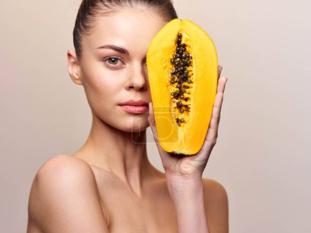 Portrait of a beautiful young woman with papaya fruit on her face, isolated on white background, skincare and beauty concept