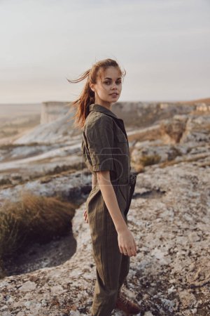 Foto de Mujer joven parada en la cima de la roca del desierto en mono verde oliva listo para la aventura - Imagen libre de derechos