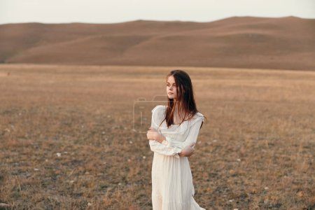 Téléchargez les photos : Belle femme en robe blanche debout dans un champ ouvert avec des montagnes majestueuses en arrière-plan, embrassant la nature et la sérénité - en image libre de droit