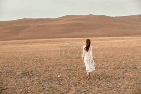 Foto de Desert wanderer a woman in a white dress exploring the remote beauty of the open field - Imagen libre de derechos