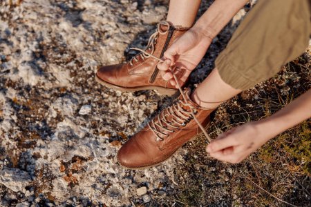 Atando cordones de zapatos en la superficie rocosa con botas marrones en la escena de aventura de viaje en el viaje de senderismo