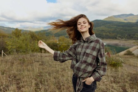 Téléchargez les photos : Une femme en chemise à carreaux debout gracieusement dans un champ balayé par le vent, mettant en valeur la beauté de la nature et de la liberté - en image libre de droit