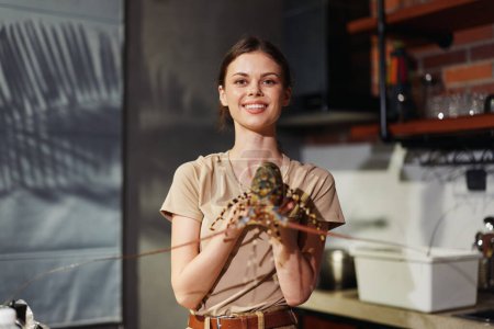 Téléchargez les photos : Woman holding a lobster in a kitchen setting, smiling and looking at the camera - en image libre de droit