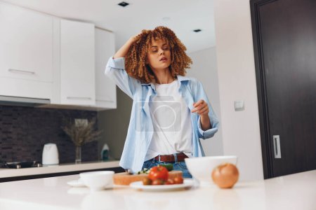 Téléchargez les photos : Une femme aux cheveux bouclés debout dans la cuisine avec une assiette de nourriture sur le comptoir - en image libre de droit
