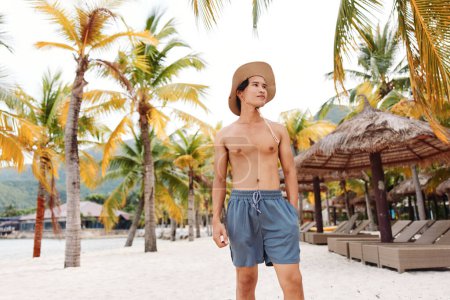 Hombre asiático sonriente en la playa tropical, disfrutando de vacaciones junto al mar