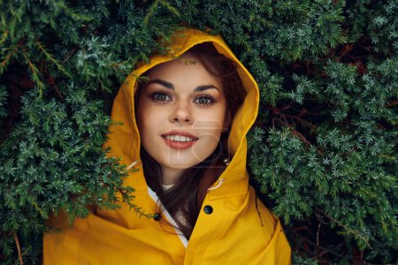 Frau in gelbem Regenmantel umgeben von immergrünen Bäumen in einem Wald bei einem Abenteuer an einem regnerischen Tag