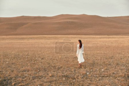 Woman walking through open field with hills in the background on travel adventure beauty journey trip meditation nature landscape beauty concept walk in nature meditation peace and serenity outdoor