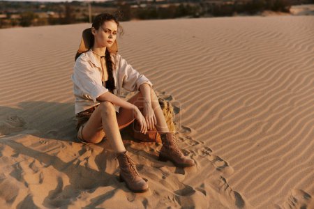 Desolate desert landscape with a woman sitting on top of a sand dune under the scorching sun