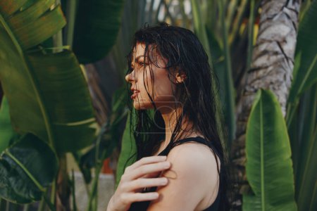 Téléchargez les photos : Belle femme aux cheveux mouillés debout devant des plantes vertes luxuriantes et des palmiers sur une oasis d'île tropicale - en image libre de droit