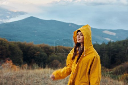 A woman in a vibrant yellow raincoat enjoying the stunning mountain views while standing on a hill