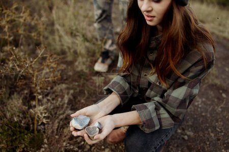 Téléchargez les photos : Une jeune femme effectuant un rituel avec un rocher à la main tandis qu'un homme se tient derrière elle observant dans la nature - en image libre de droit