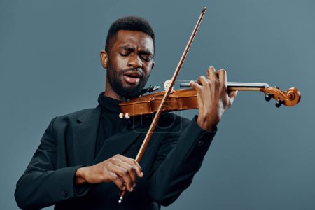 Talented African American man in black suit showcasing his violin skills against a neutral gray backdrop