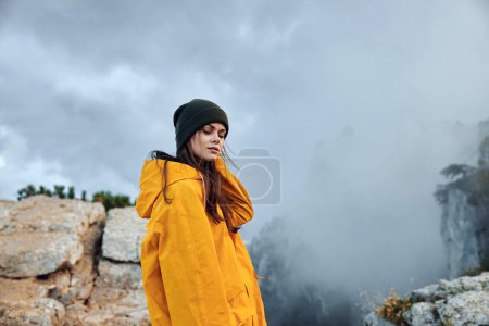 Woman in Yellow Raincoat Contemplating the Beauty of Nature on Top of Misty Mountain Summit Amidst Foggy Landscape