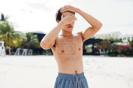 Hombre asiático musculoso disfrutando de unas vacaciones en la playa: sonriente, sin camisa y feliz en el paraíso tropical
