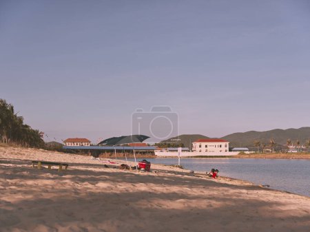 Foto de Escena de playa de arena con cometa y gente sentada cerca de ella en un día soleado - Imagen libre de derechos