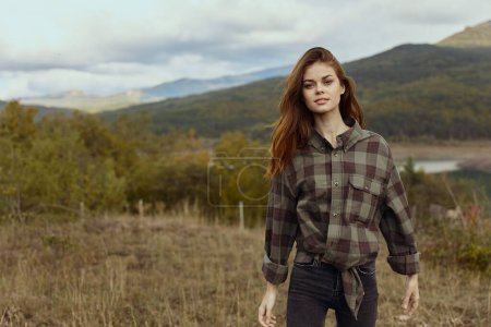 Photo for Young woman in plaid shirt and jeans standing confidently in the middle of a scenic field during a travel adventure - Royalty Free Image