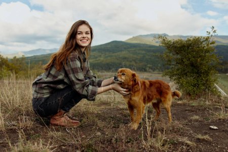 Woman bonding with her loyal companion in a serene field amidst majestic mountains in a peaceful travel moment