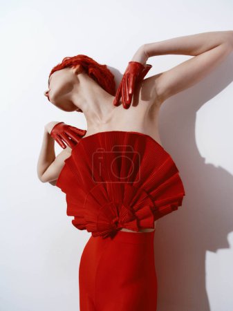 Femme confiante en tenue rouge élégante posant avec les mains sur la tête sur fond blanc