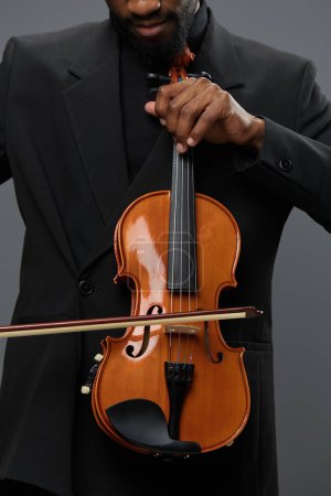 An elegant African American man in a suit holding a violin on a neutral gray background