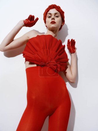 Femme élégante en robe rouge et gants posant contre le mur blanc pour le portrait photoshoot de mode