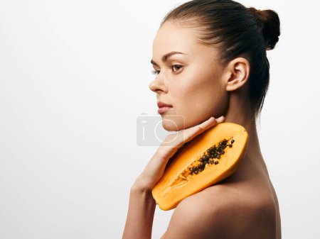 Mujer joven con piel brillante sosteniendo fruta madura de papaya sobre fondo blanco para la belleza natural y el concepto de bienestar