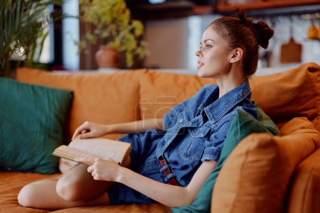 Femme lisant un livre sur un canapé en jean et chemise