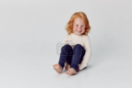 Adorable redhaired girl sitting on floor in front of white background childhood beauty and innocence portrait