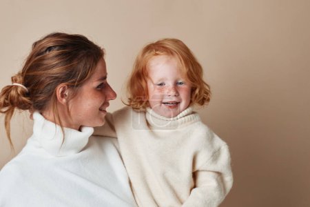 Mutter und Tochter in passenden weißen Pullovern lächeln in die Kamera, Familienfotosession schöne Momente eingefangen