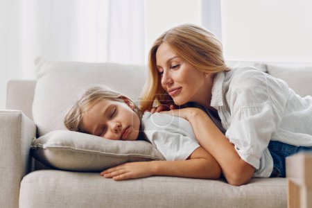 Madre e hija relajándose en un sofá juntas en un luminoso ambiente minimalista de sala de estar