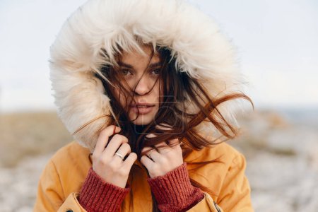 Young woman in yellow jacket with fur hood standing in the middle of field embracing the beauty of nature