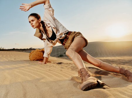 Frau in braunem Hemd und kurzen Hosen steht auf einer Sanddüne in der Wüste unter strahlend blauem Himmel